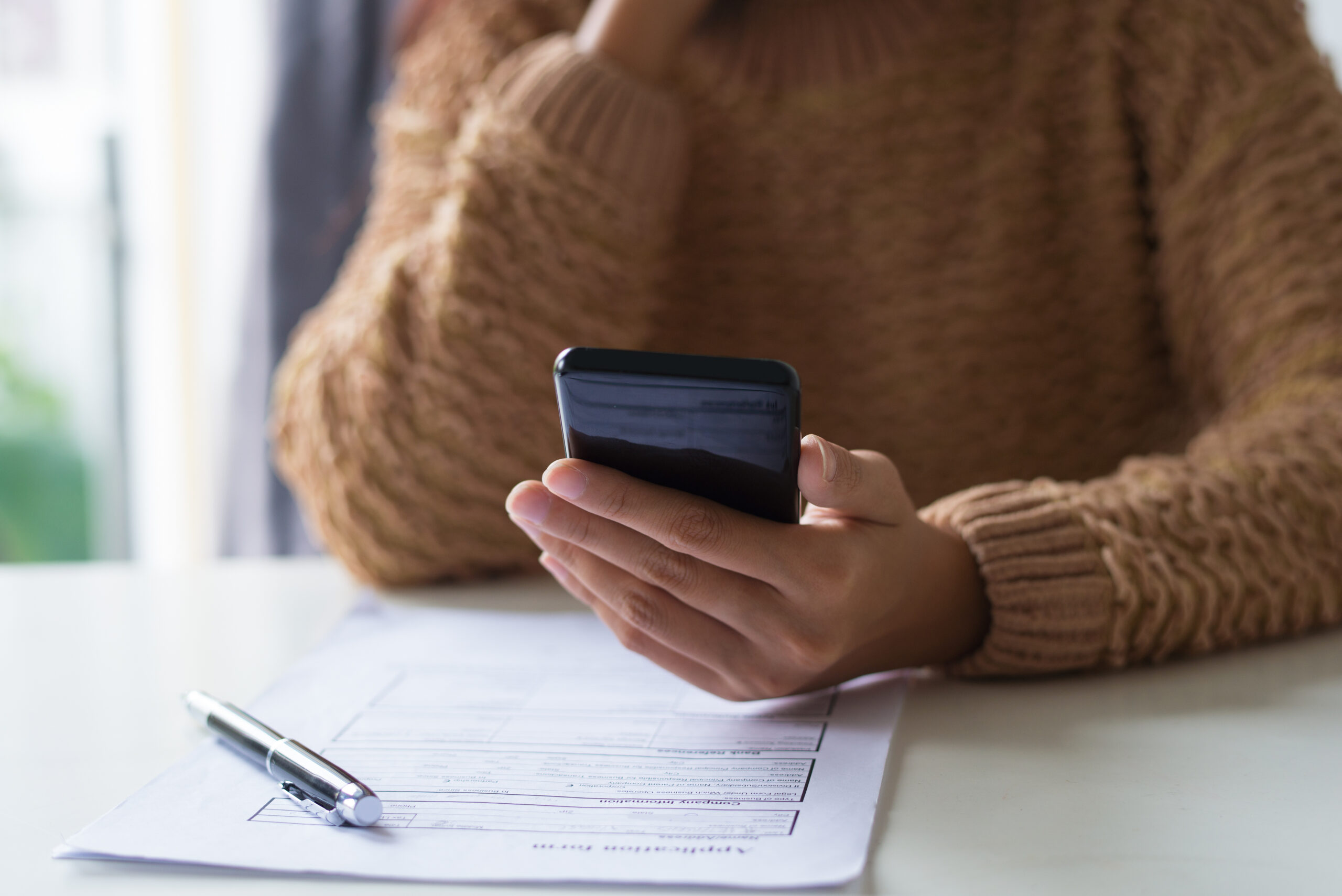 Gros plan d'une dame occupée remplissant un document et vérifiant son téléphone